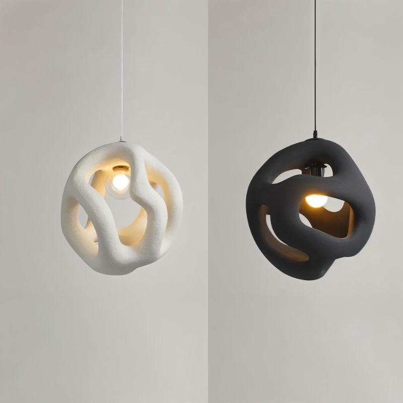 Clérachic white and black openwork pendant lights side by side on a pale grey backdrop, each lit by a warm bulb.