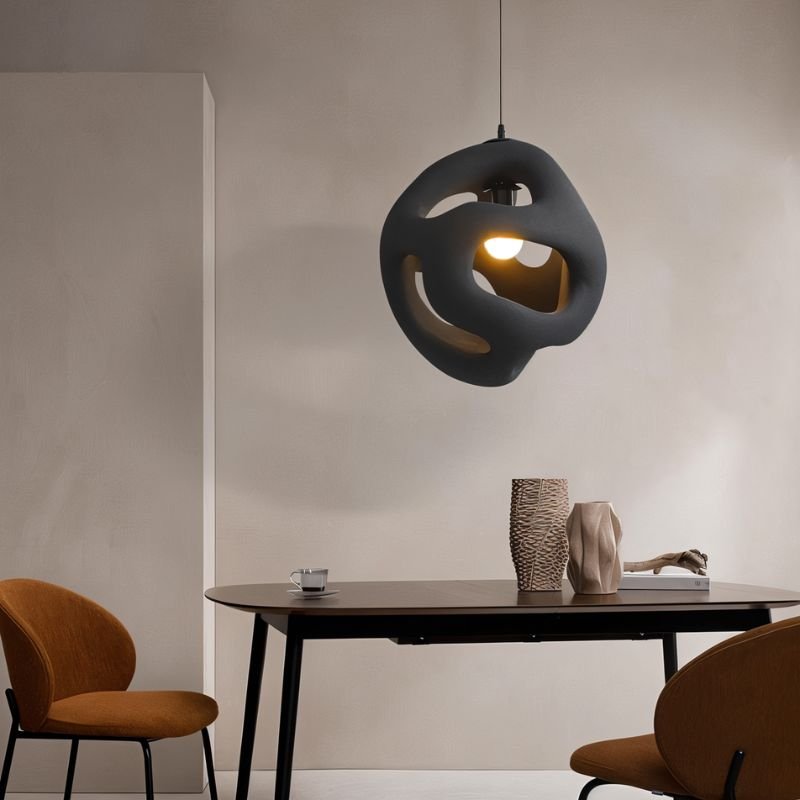 Clérachic black openwork pendant light hanging over a dark dining table with two rust-coloured chairs and ceramic vases.