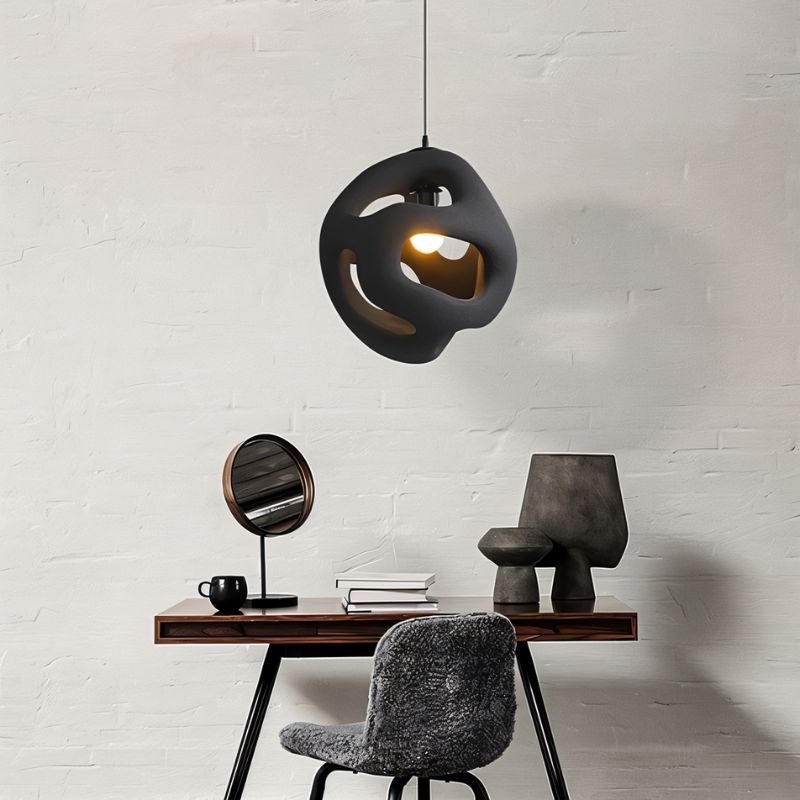 Clérachic black openwork pendant light hung above a small wooden desk, mirror and ceramic vases against a white brick wall.