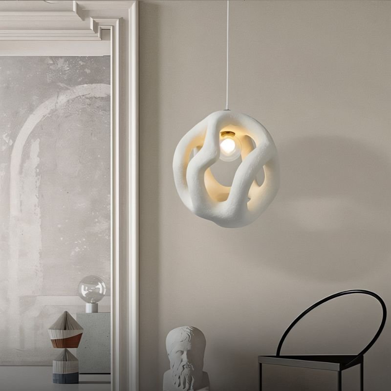 Clérachic white openwork pendant light glowing beside a panelled doorway, with a plaster bust and a black arched chair below.