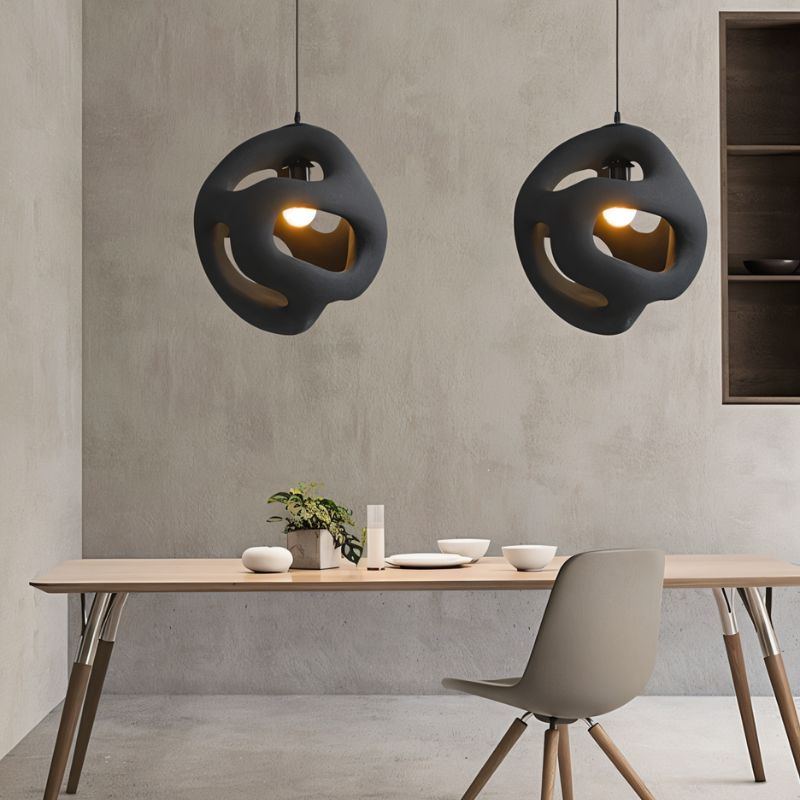 Clérachic pair of black openwork pendant lights above a pale wood dining table and grey chair against a concrete-effect wall.