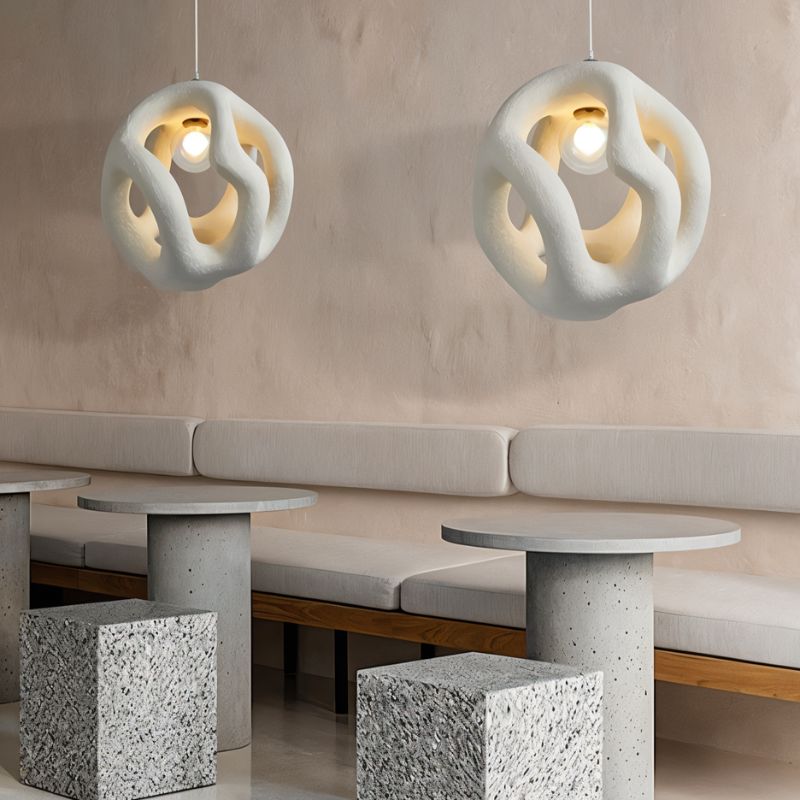 Clérachic pair of white openwork pendant lights glowing over round concrete tables and a cushioned banquette.