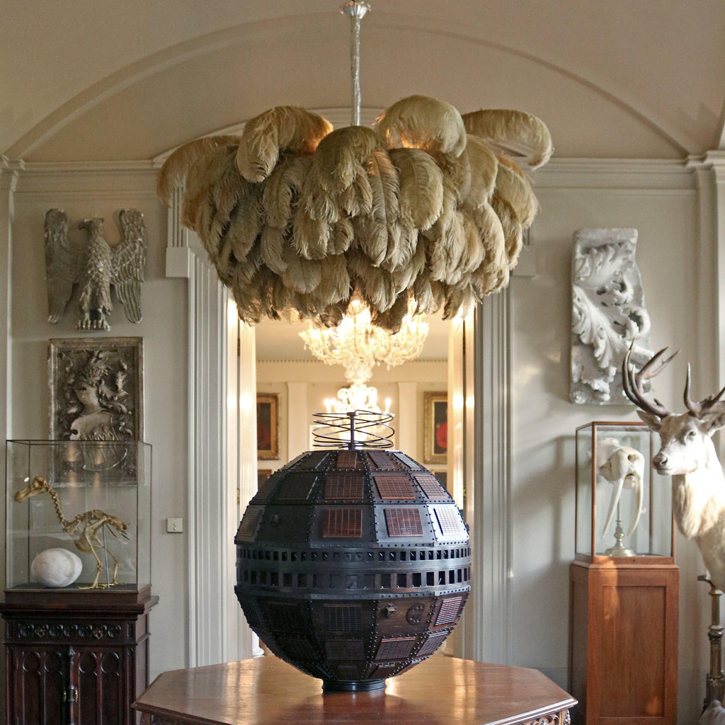 Natural-toned ostrich feathers form a full, layered canopy on this Clérachic chandelier, hung in a high-ceilinged room with stone reliefs.