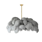 Light grey feathers cascade in thick layers from the brass stem of this Clérachic chandelier, shown on white.