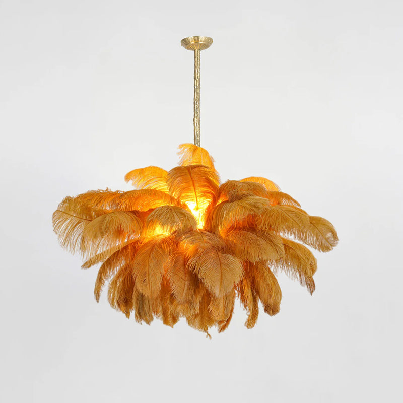 Amber-orange feathers glow around the lit centre of this Clérachic chandelier, its brass stem set against a soft grey backdrop.