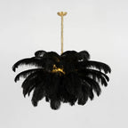 A black-feather Clérachic chandelier is lit at its core, hung from a short brass stem against a pale grey wall.