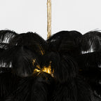 Close view of black feathers around the lit core of this Clérachic chandelier, with the brass stem at the top.