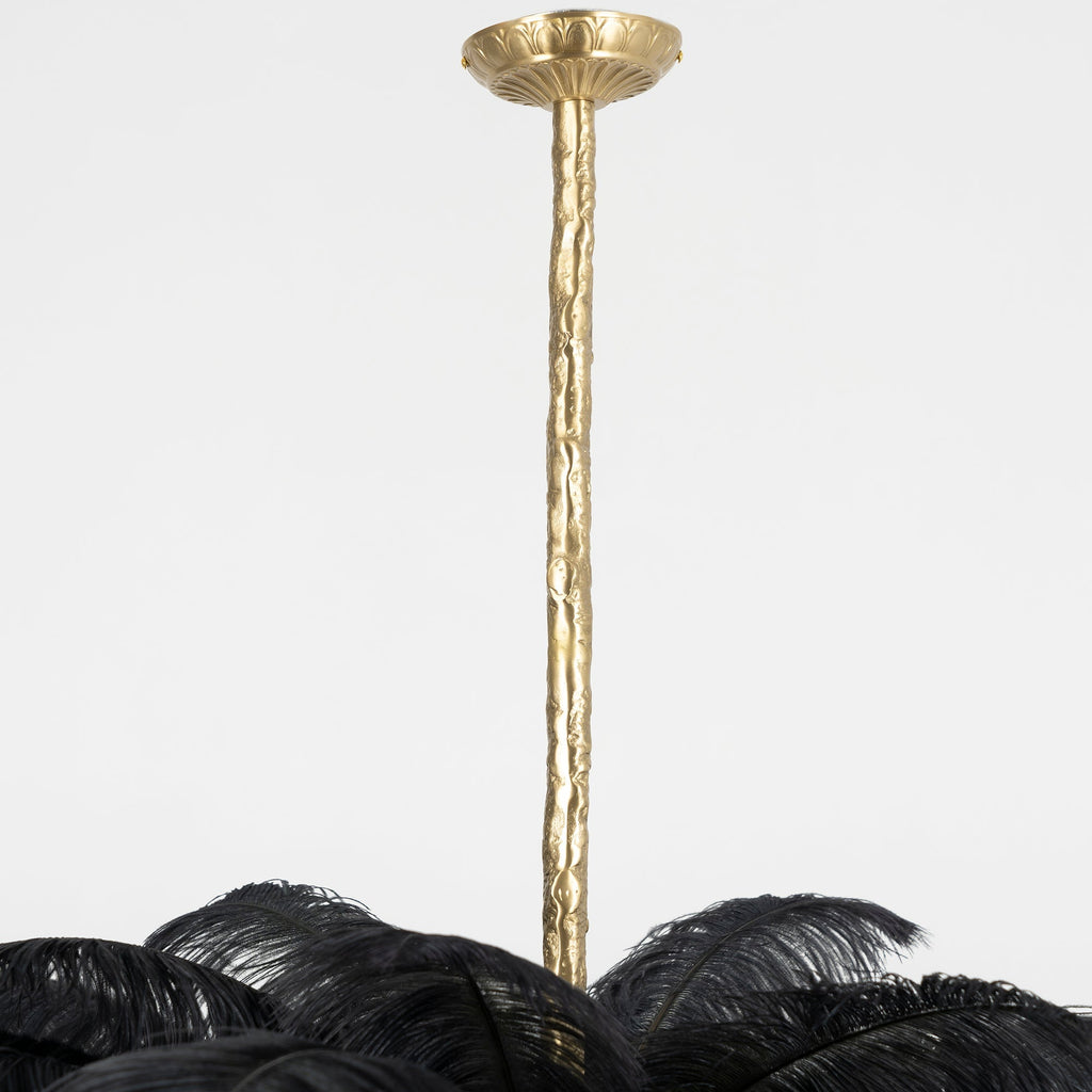 Close view of the carved brass stem and round ceiling canopy of this Clérachic chandelier, with black feathers below.