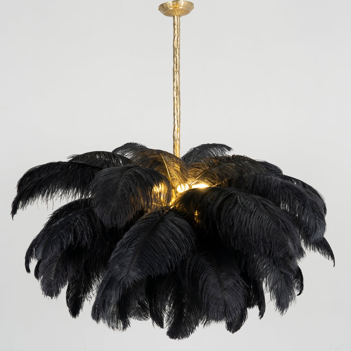 A black-feather Clérachic chandelier glows from within, with its brass stem rising to a grey ceiling.
