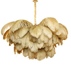 Gold-toned feathers with darker tips layer thickly on this Clérachic chandelier, from a brass stem on white.