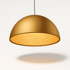 Clérachic gold dome pendant light switched on, its relief-patterned interior glowing a warm amber.