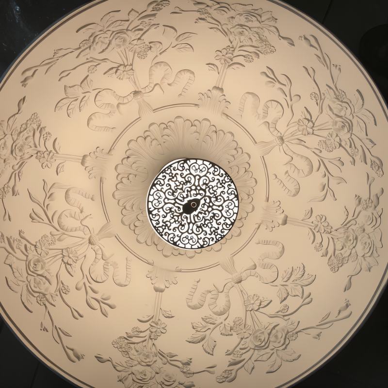 Looking up into a Clérachic dome pendant, the pale interior moulded with floral relief around a filigree disc.