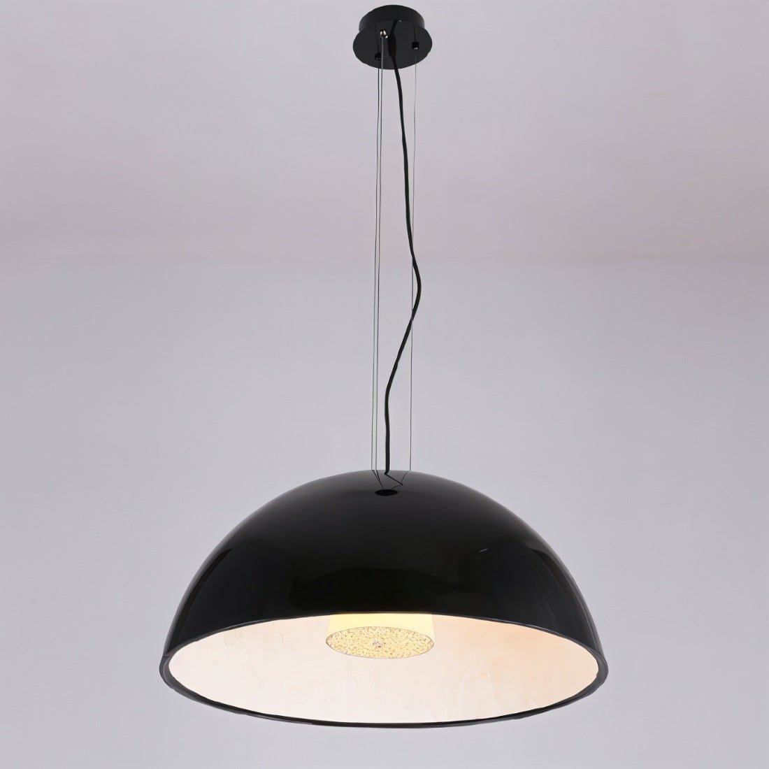 Clérachic glossy black dome pendant light hung on fine wires and a black cord, glowing warm inside, on grey.