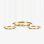 Four gold rings of different diameters hang at staggered heights on thin cables against a white backdrop, on this Clérachic ring pendant.
