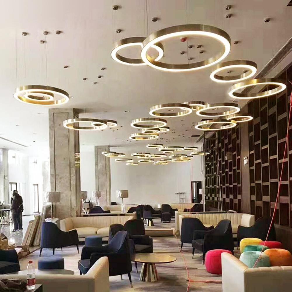 Many gold ring pendants at different heights fill the ceiling of a large open lounge with navy armchairs, in the style of this Clérachic ring pendant.