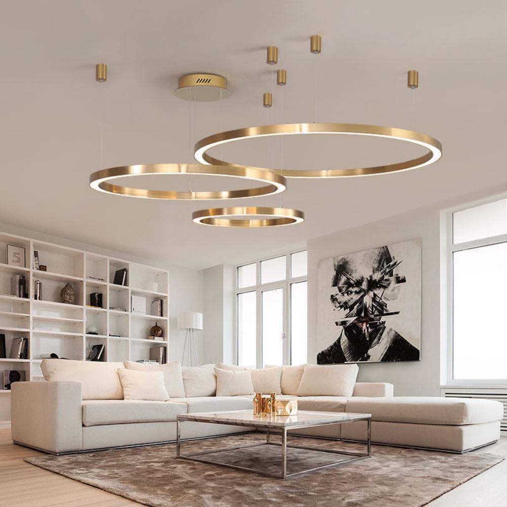 Four brushed gold rings hang from small ceiling canopies over a cream sofa and a white bookcase, a living room lit by this Clérachic pendant.