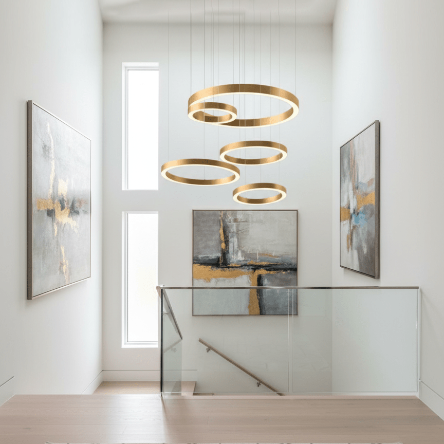 Five gold rings hang at varied heights in a white double-height stairwell between two abstract paintings, shown with this Clérachic ring pendant.