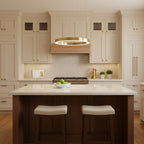 A single gold ring hangs above a white kitchen island with two stools and cream cabinets, lit by this Clérachic ring pendant.