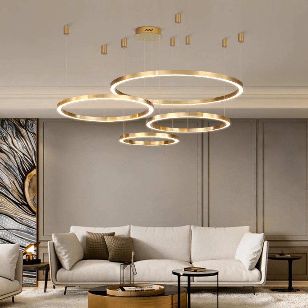 Five brushed gold rings hang from a ceiling plate above a cream sofa in a living room with panelled walls, lit by this Clérachic pendant.