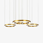 Four gold rings of varied sizes hang from fine cables against a plain pale backdrop, shown as one Clérachic ring pendant.