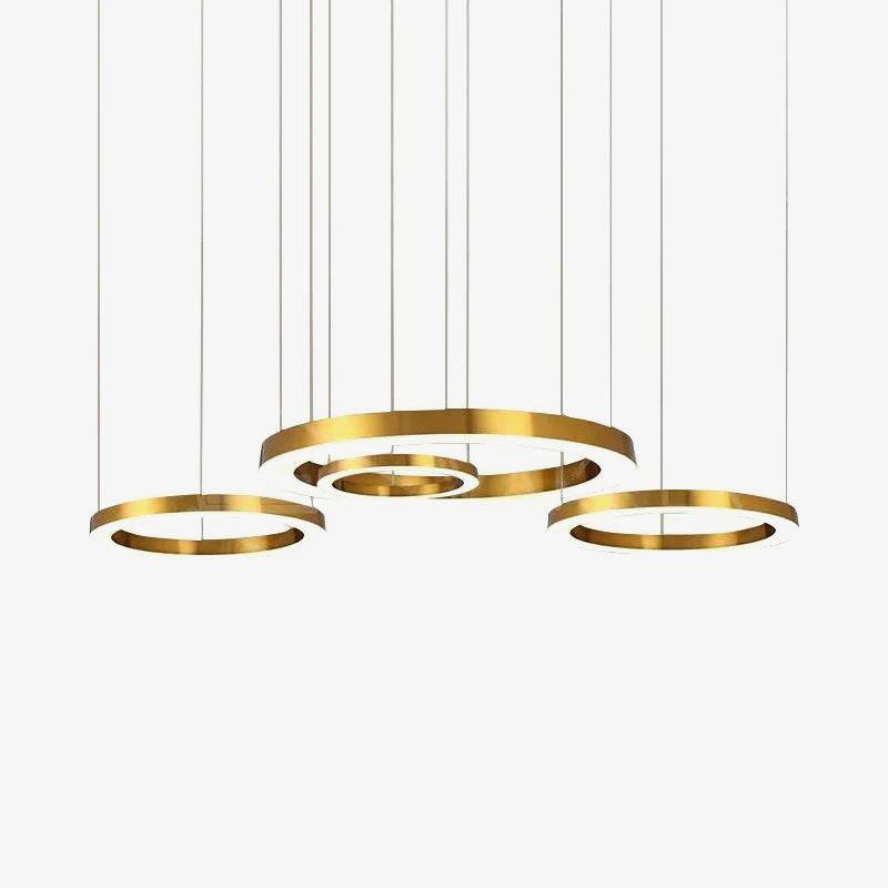 Four gold rings of varied sizes hang from fine cables against a plain pale backdrop, shown as one Clérachic ring pendant.