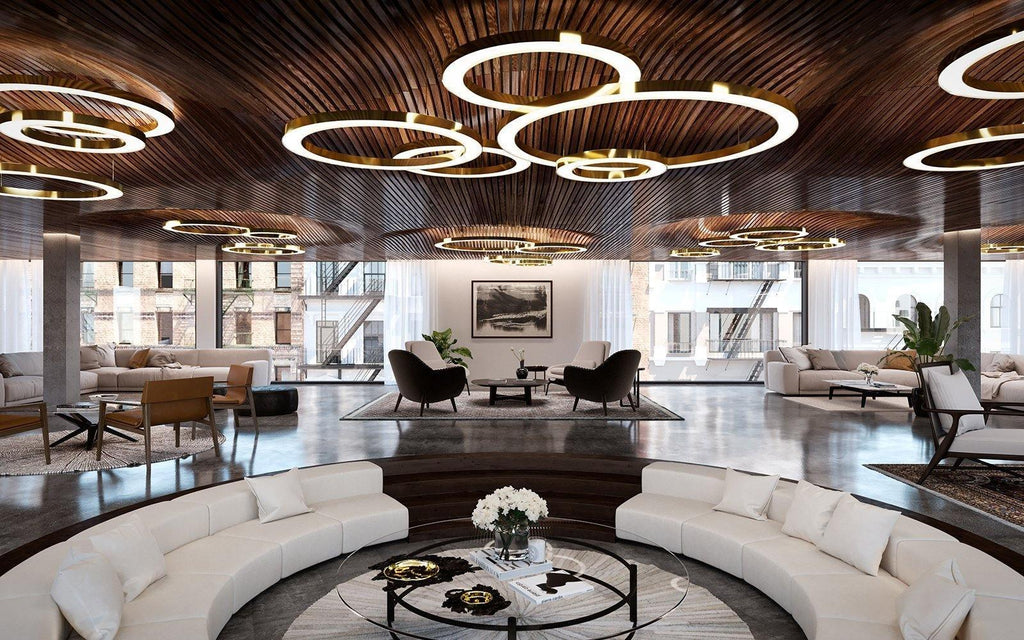 Lit gold rings hang in overlapping groups below a timber-slat ceiling in a wide lounge with curved white seating, in a Clérachic ring pendant setting.