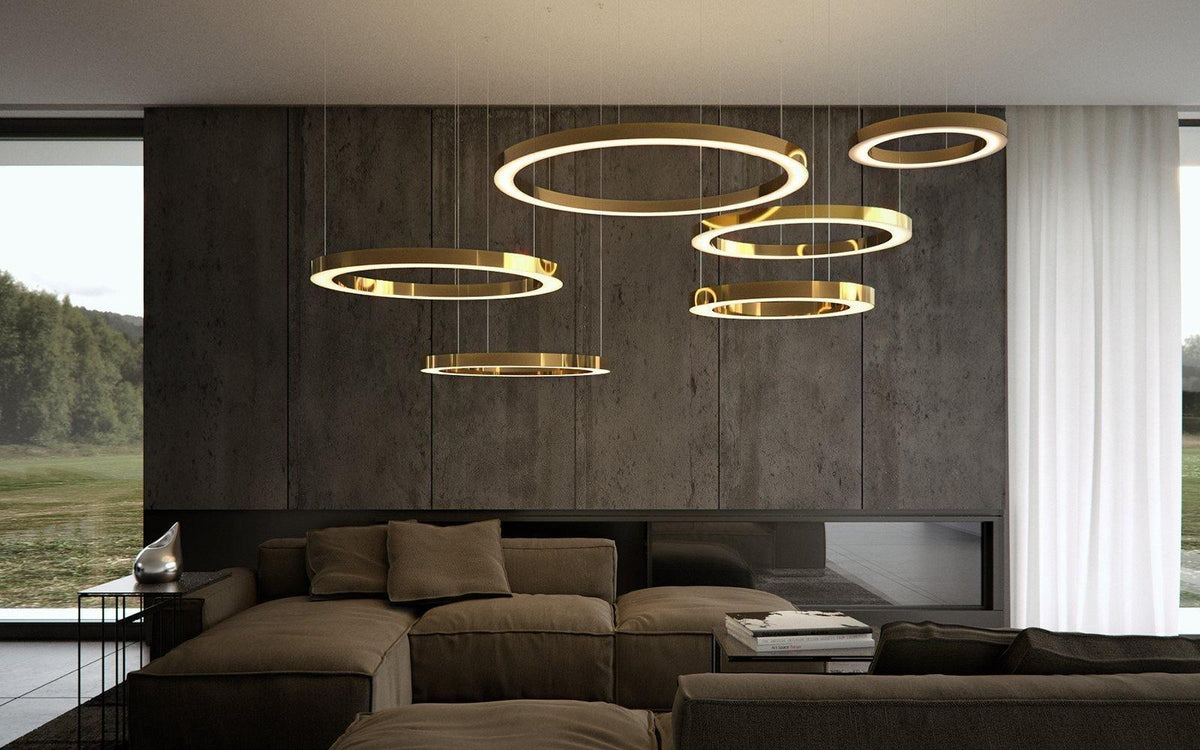Gold rings at different heights hang in front of a dark stone feature wall and a window onto green hills, shown with this Clérachic pendant.