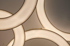 Close view of overlapping glowing rings with thin gold edges, showing the soft light of this Clérachic ring pendant against a ceiling.