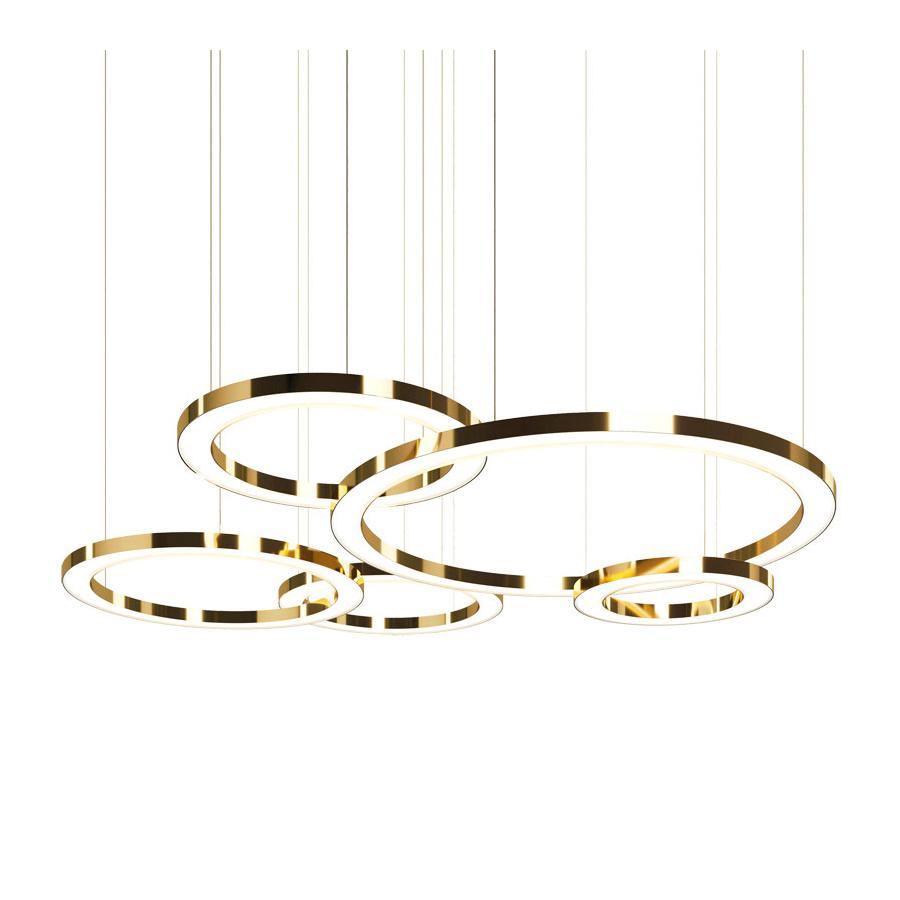Five polished gold rings of different diameters hang from fine cables on a white backdrop, with the glowing inner faces of this Clérachic pendant.