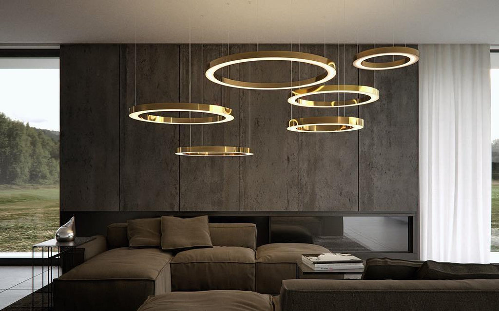 Gold rings hang at staggered heights over a dark lounge with a stone-clad wall and a window onto trees, lit by this Clérachic pendant.