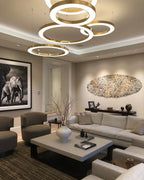 Overlapping lit gold rings hang low in a living room with two armchairs, a pale coffee table and a large framed photograph, from Clérachic.
