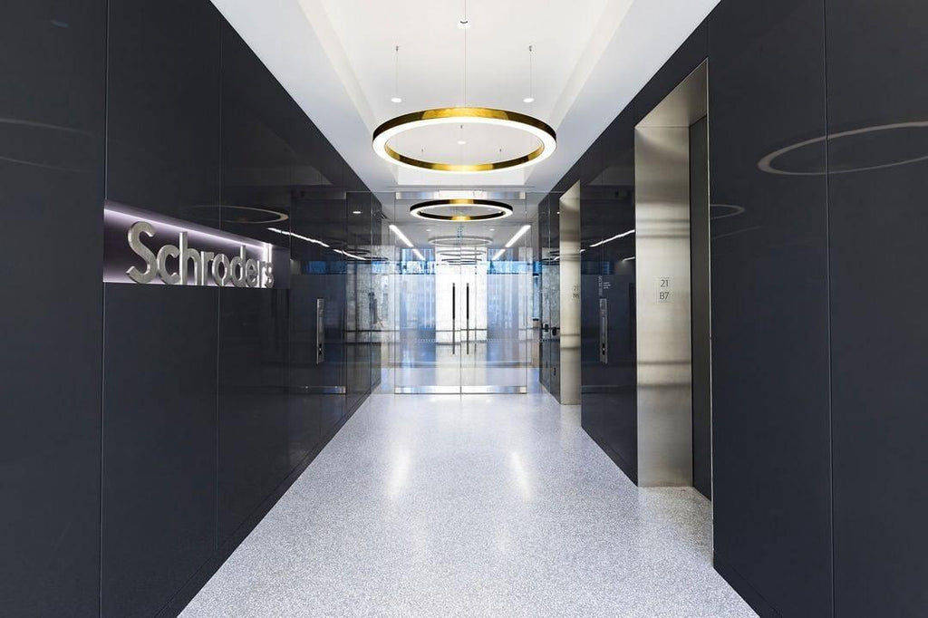 Two gold rings hang in a dark corridor with a polished floor that leads toward glass doors, lit by this Clérachic ring pendant.