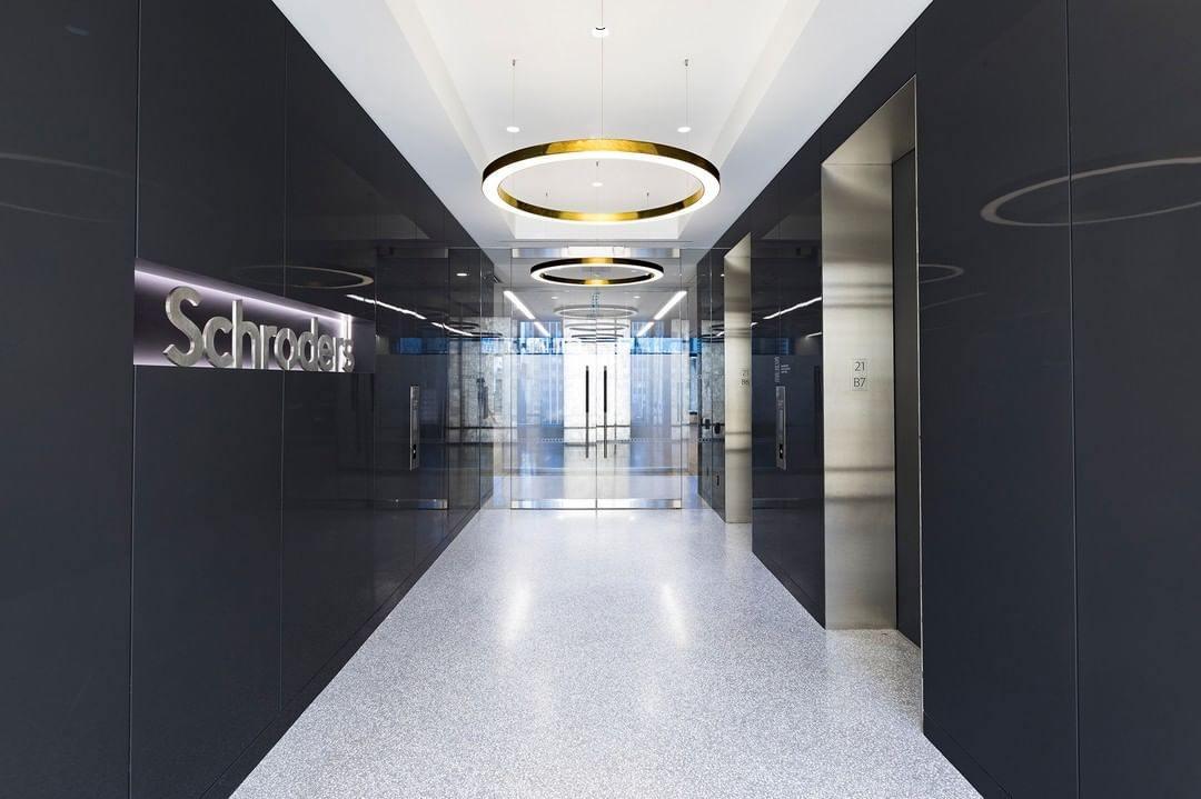 Two gold rings hang in a dark corridor with a polished floor that leads toward glass doors, lit by this Clérachic ring pendant.