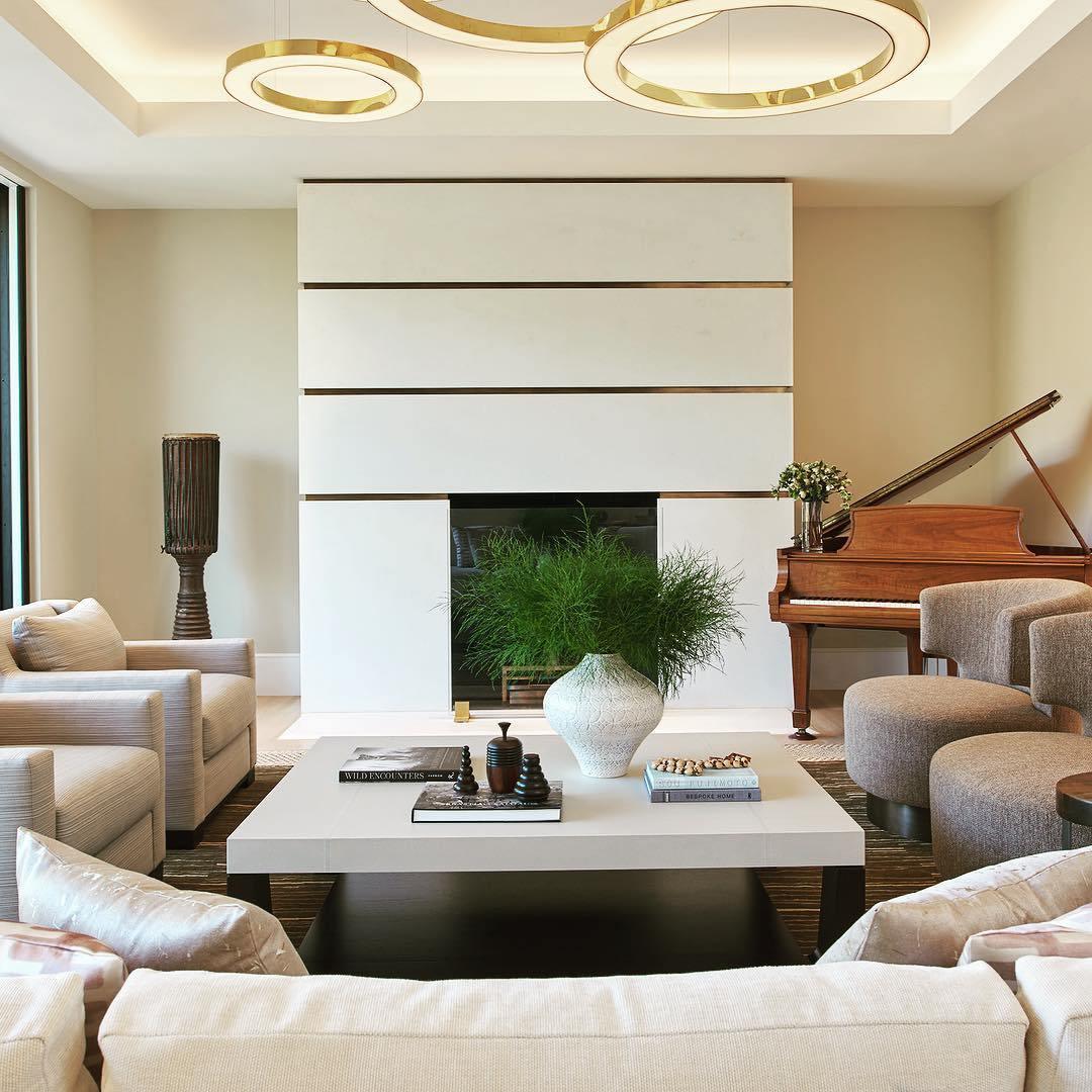 Gold ring edges glow at the top of the frame above a white sofa, a fireplace wall and a grand piano, with this Clérachic ring pendant overhead.