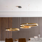 Three gold rings hang from a round ceiling plate above a marble counter, against a wall of slim timber slats, lit by this Clérachic pendant.