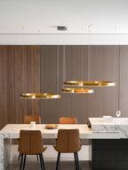 Three gold rings hang at different heights against a walnut-slat wall, above a marble counter and tan leather chairs, from Clérachic.