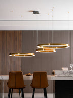 Three gold rings hang below a round ceiling plate, with tan leather chairs and a wine glass on a marble counter, lit by this Clérachic pendant.
