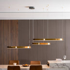 Side view of three flat gold rings hanging at different heights against a slatted wall, above a counter with tan chairs, a Clérachic pendant.