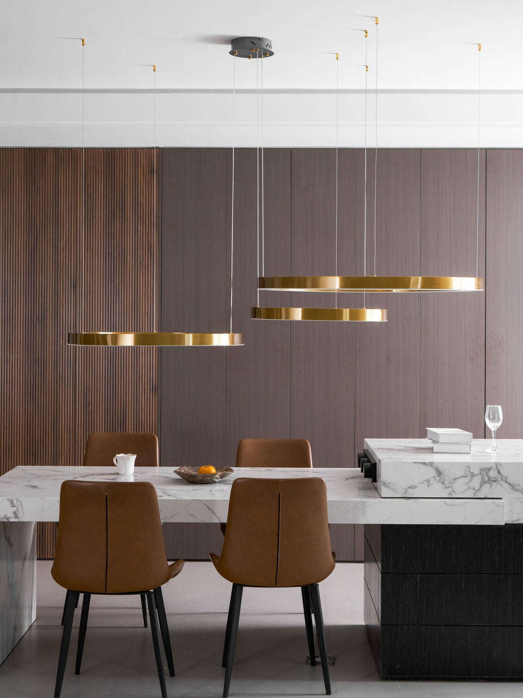 Three gold rings hang at an eye-level angle above a marble dining counter with tan chairs and a wine glass, shown as this Clérachic pendant.