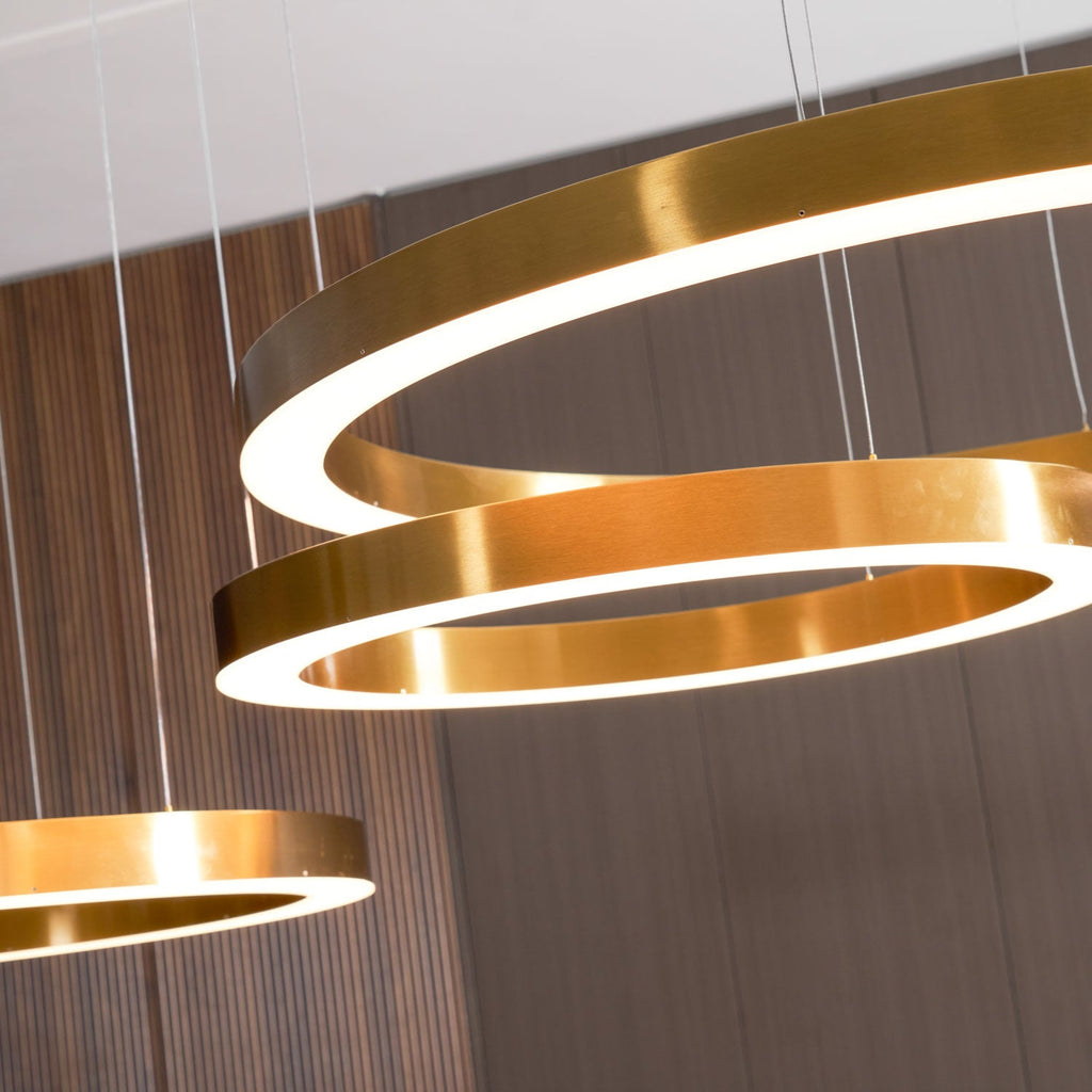 Close view of brushed gold ring edges with the white glow of the diffuser, against a walnut-slat wall, on this Clérachic ring pendant.