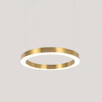 A single gold ring hangs on three fine cables against a plain pale grey backdrop, its white diffuser glowing, from Clérachic.