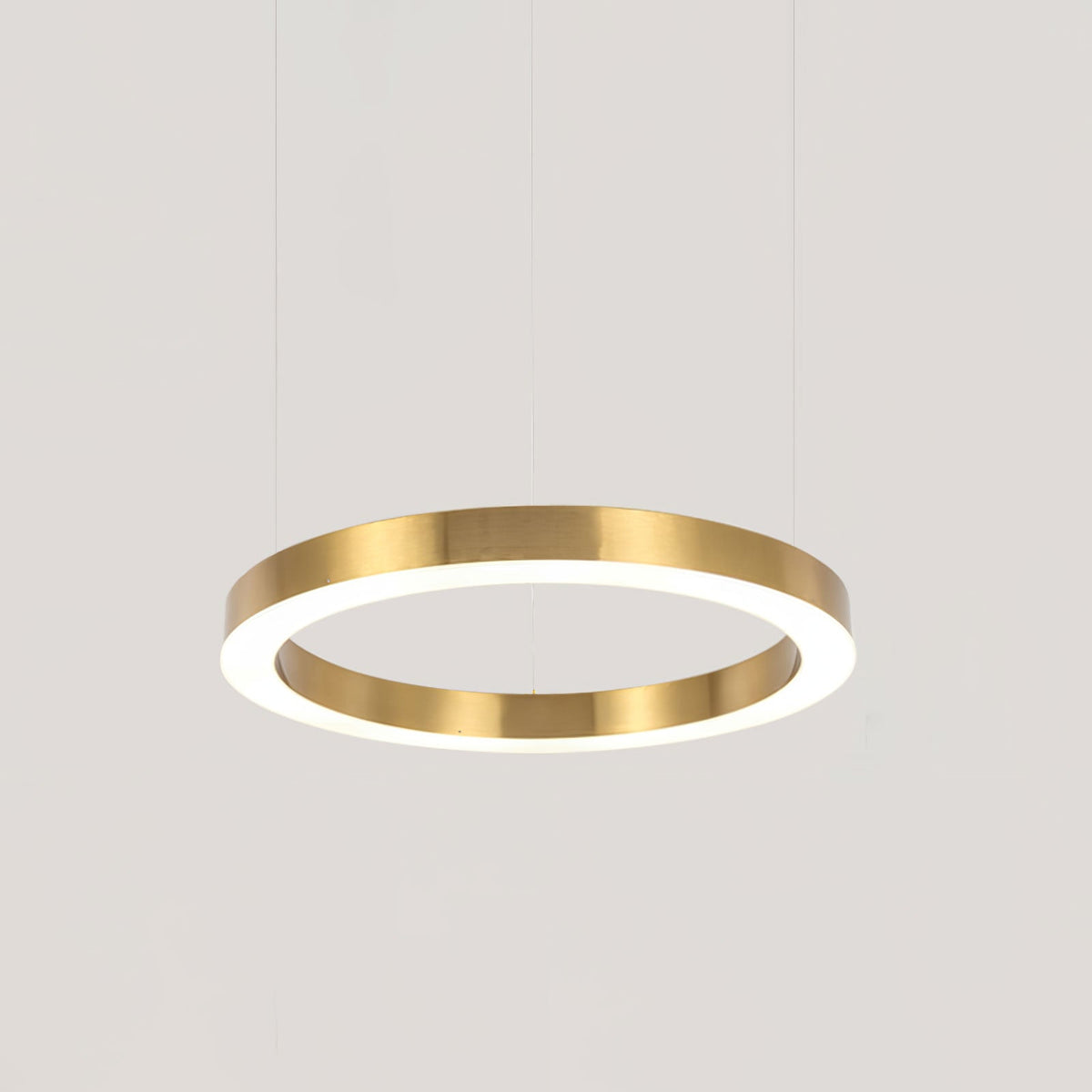 A single gold ring hangs on three fine cables against a plain pale grey backdrop, its white diffuser glowing, from Clérachic.