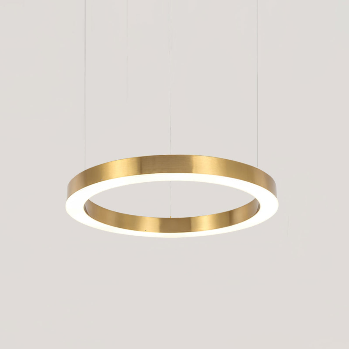 A larger single gold ring with a glowing white diffuser hangs on cables against a pale grey backdrop, shown as this Clérachic pendant.
