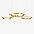 Three gold rings hang from fine cables against white, the two outer rings below a larger pair, with this Clérachic ring pendant switched on.