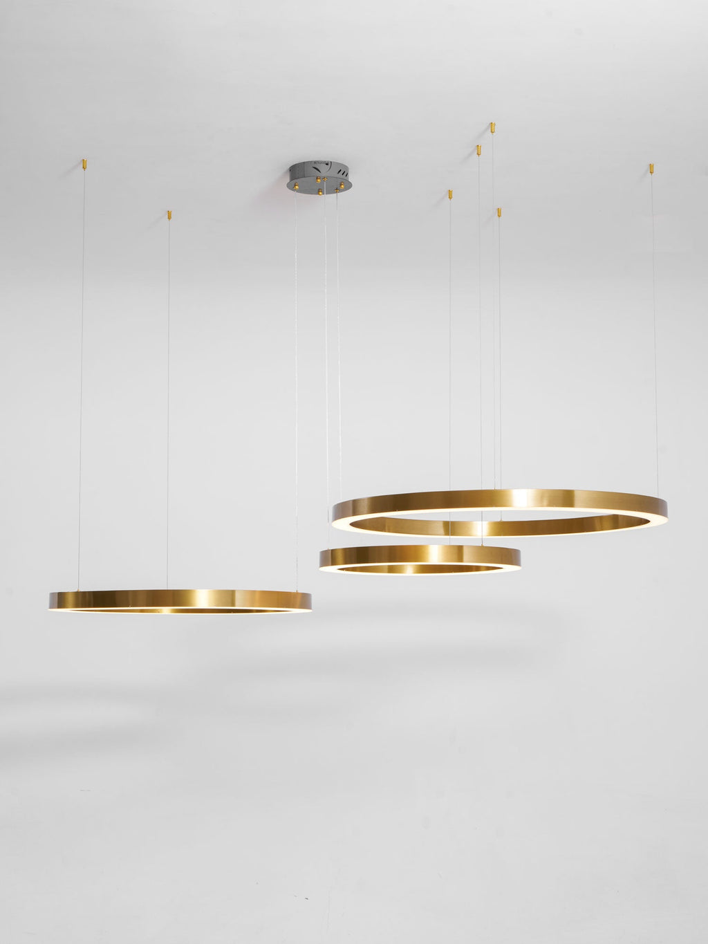 Four brushed gold rings hang at varied heights from a grey ceiling canopy against a pale studio backdrop, from Clérachic.