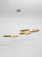 Four brushed gold rings hang at varied heights from a grey ceiling canopy against a pale studio backdrop, from Clérachic.