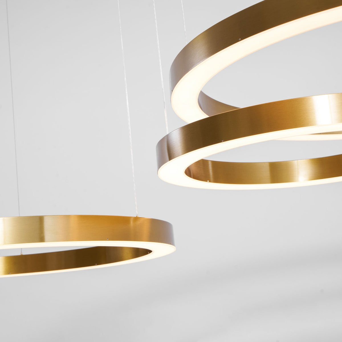 Close view of gold ring edges with the lit white diffuser inside each ring, against a soft grey backdrop, on this Clérachic pendant.