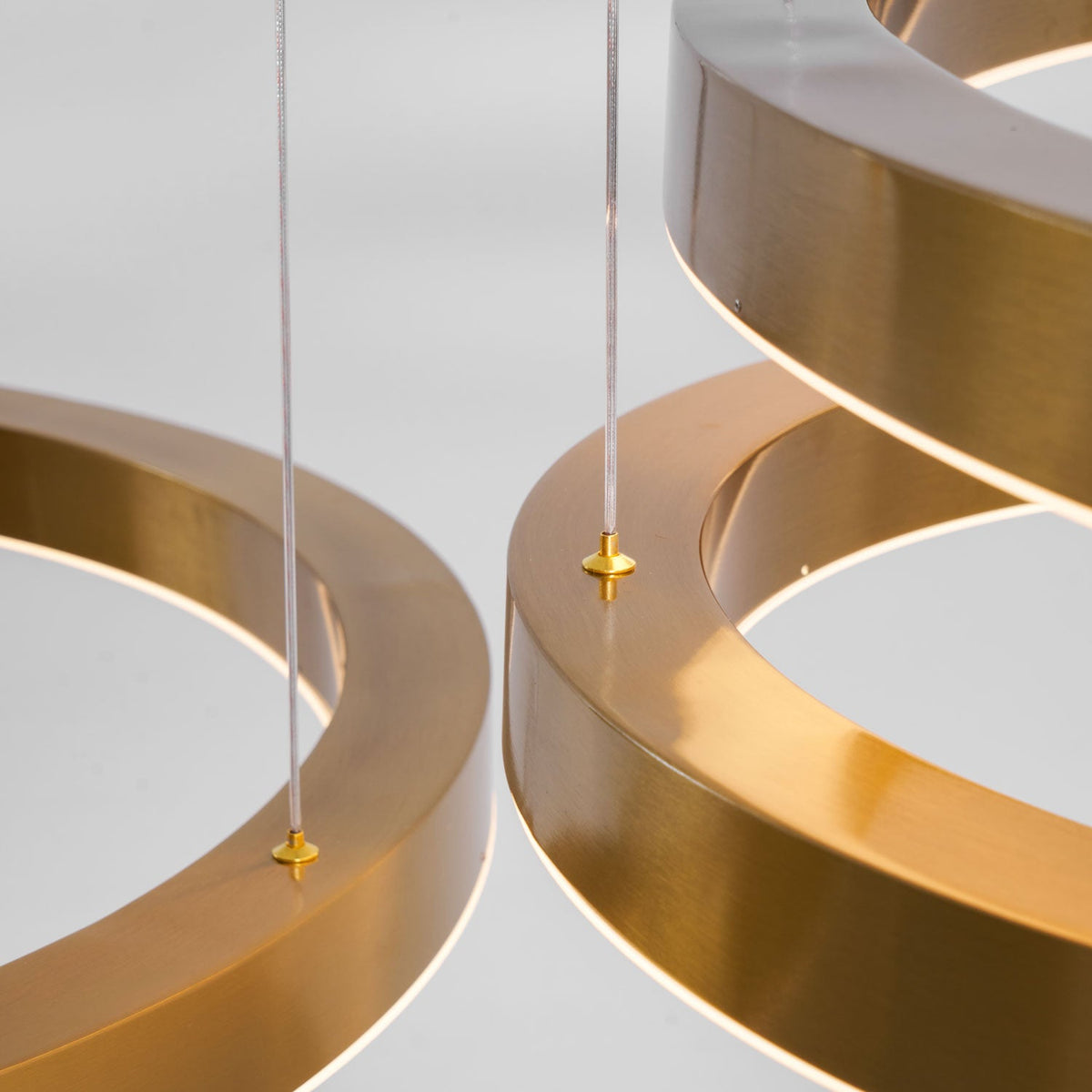 Close view of two gold ring edges with small brass cable fixings holding the thin suspension cable, on this Clérachic ring pendant.