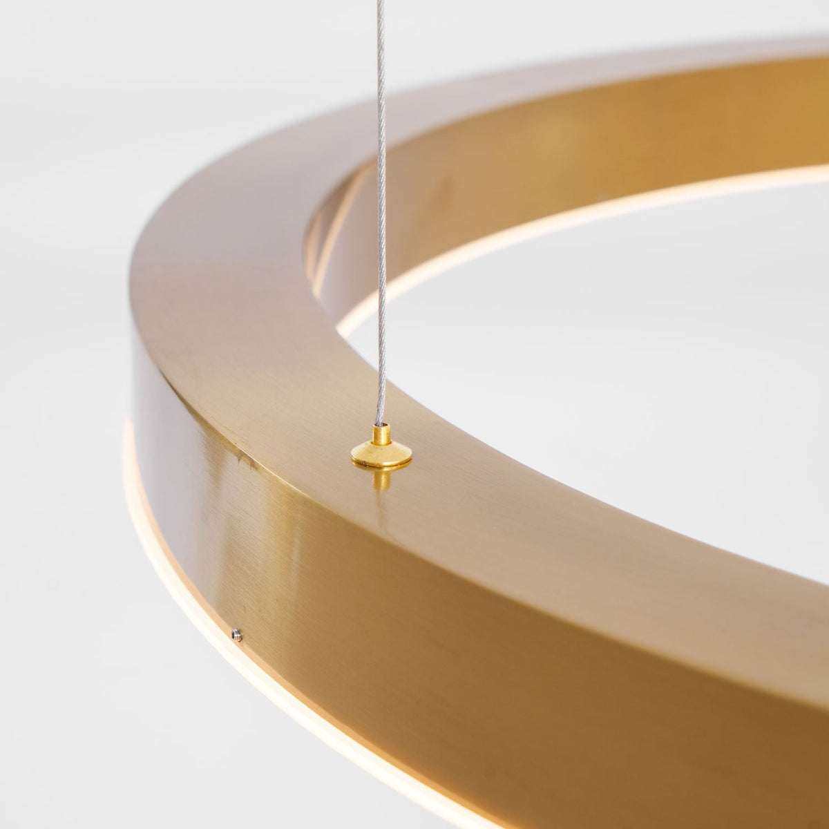 Close view of a brushed gold ring with a brass cable gripper on top and the white light strip beneath, on this Clérachic pendant.