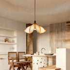 A Clérachic petal-shaped pendant lit above a kitchen island with rattan chairs, wood panelling and cream plaster walls.